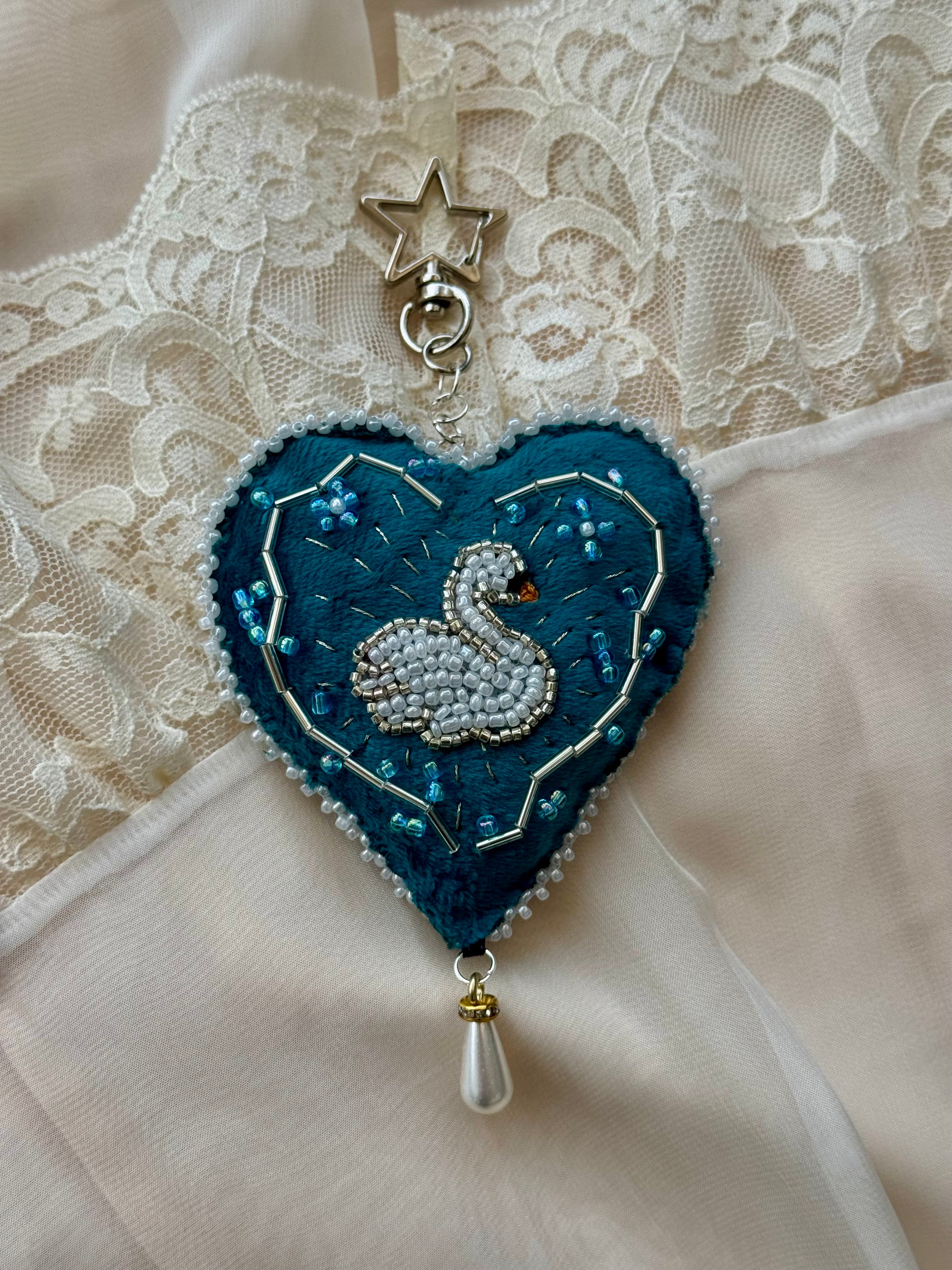 Heart-shaped decorative item with a beaded swan design on a lace background