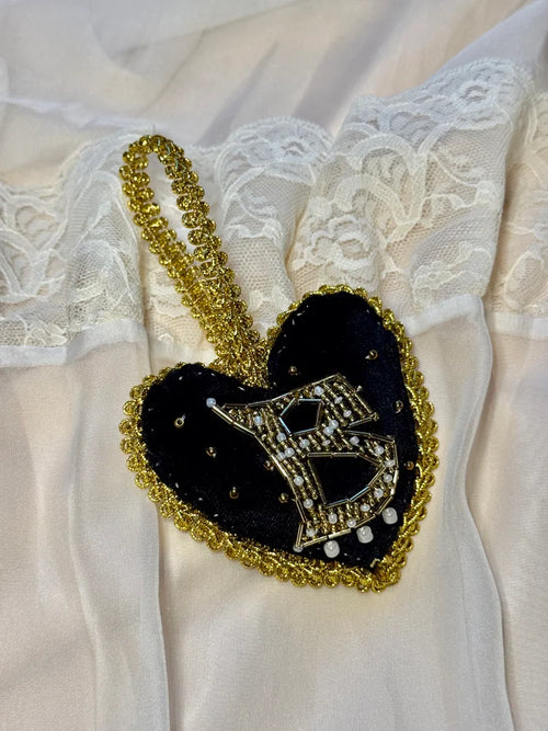 Heart-shaped brooch with gold and black design on a white lace fabric background