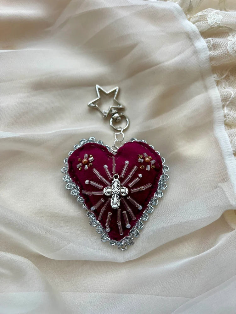Heart-shaped embroidered pendant with a cross on a white fabric background