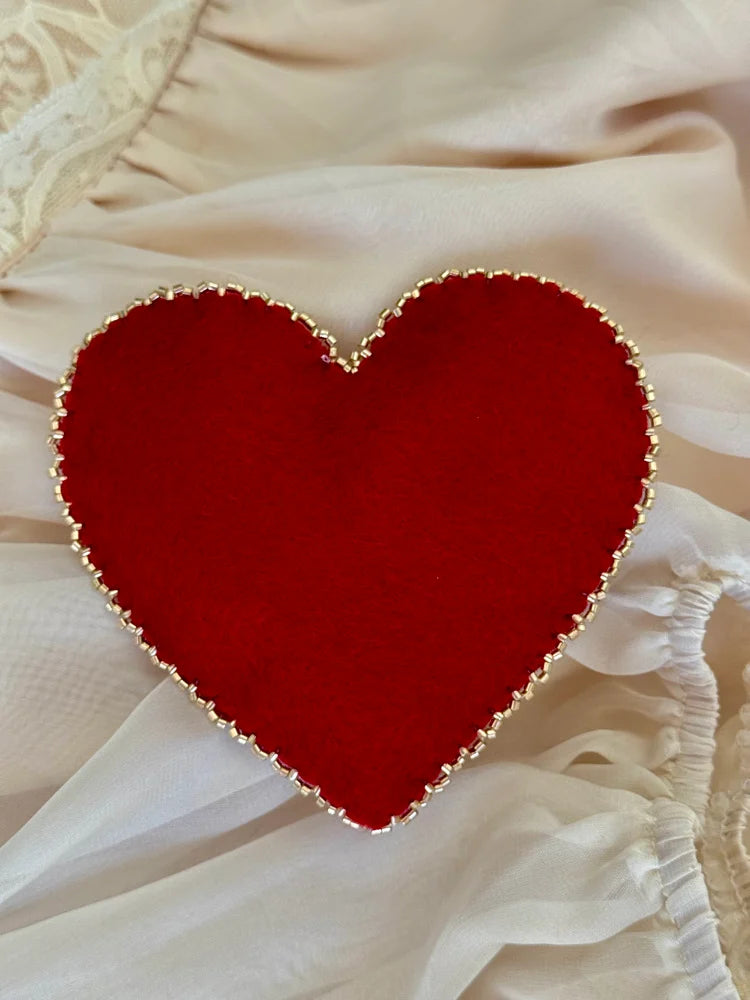 Red heart-shaped object with gold trim on a beige fabric background