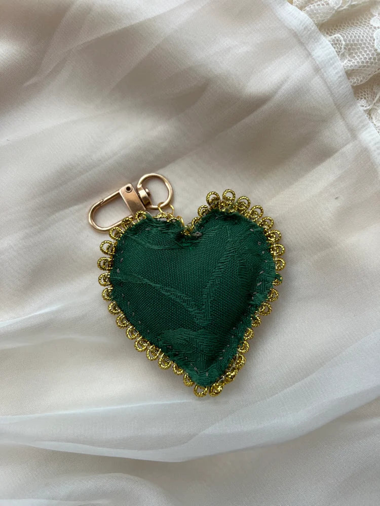 Green heart-shaped keychain with gold trim on a white fabric background