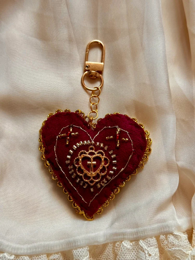 Heart-shaped keychain with gold embroidery on a beige fabric background