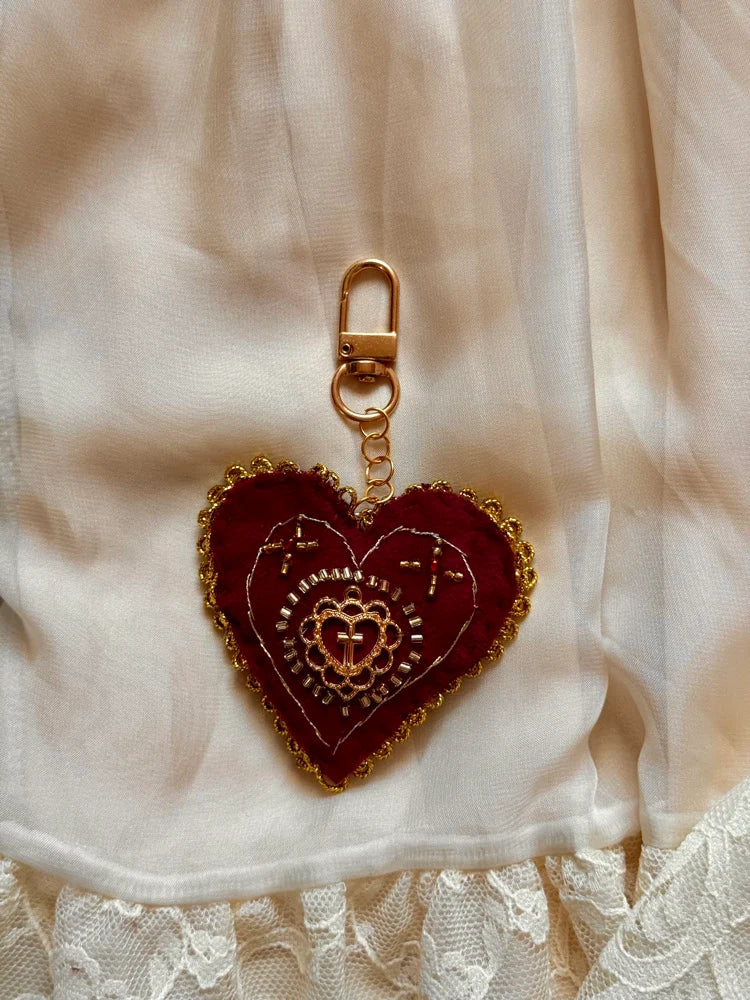 Heart-shaped keychain with gold embroidery on a soft fabric background
