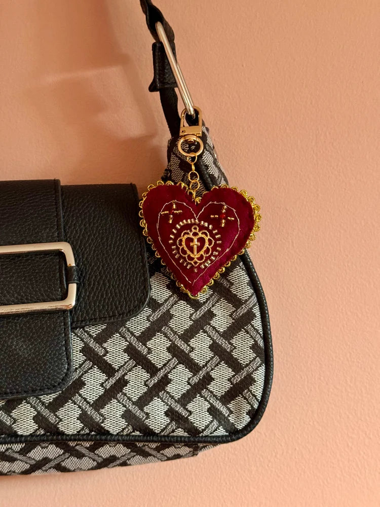 Heart-shaped keychain with gold accents on a patterned handbag against a peach background