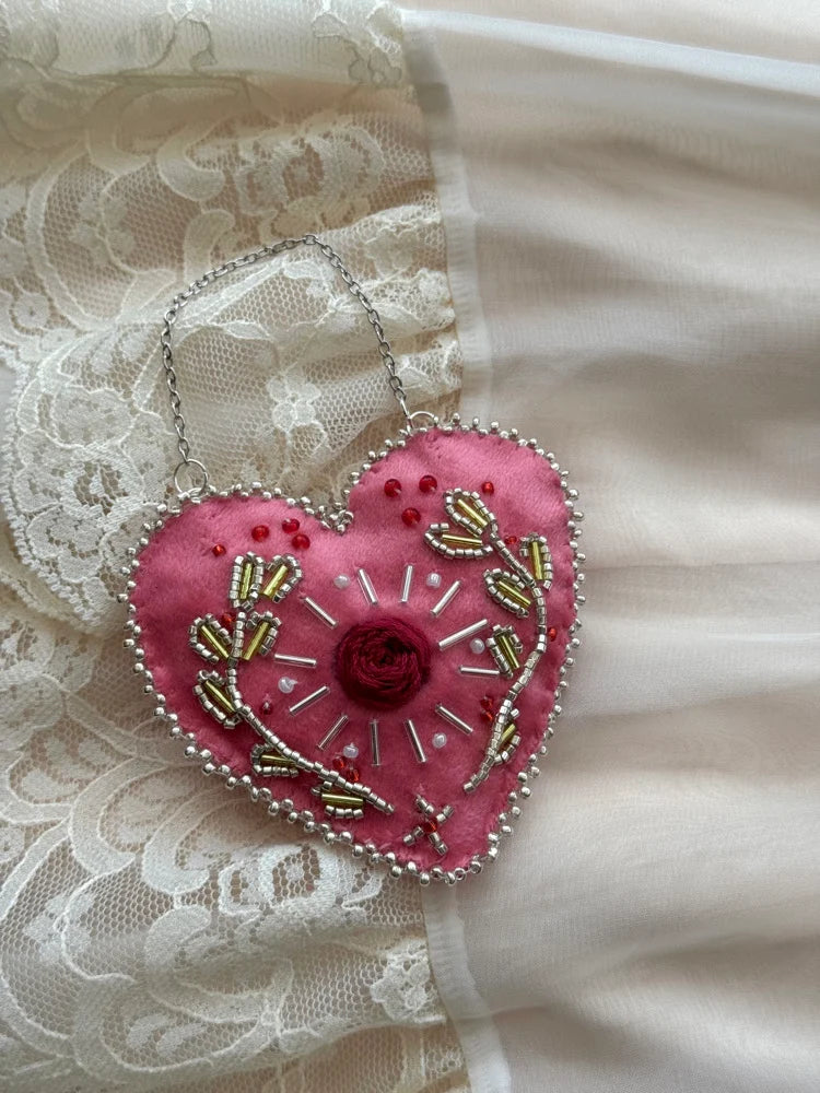 Pink heart-shaped embroidered pendant on a lace fabric background