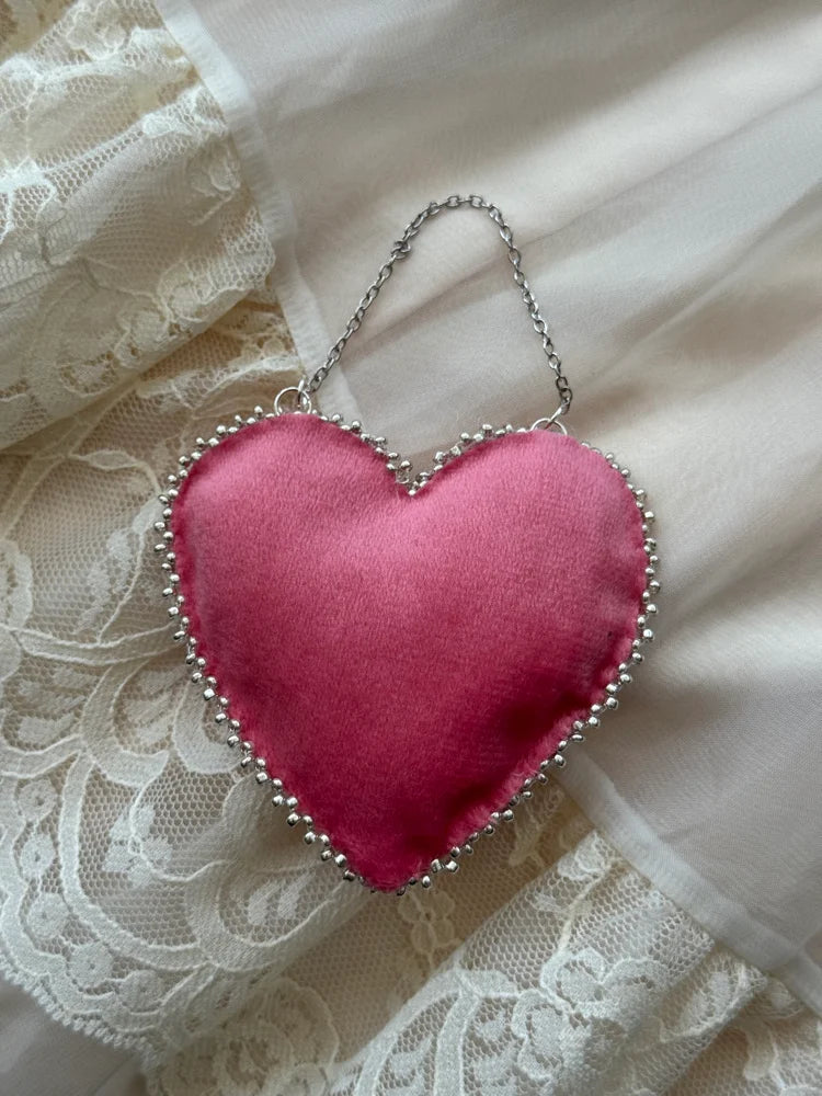 Pink heart-shaped fabric ornament with a chain on a lace background