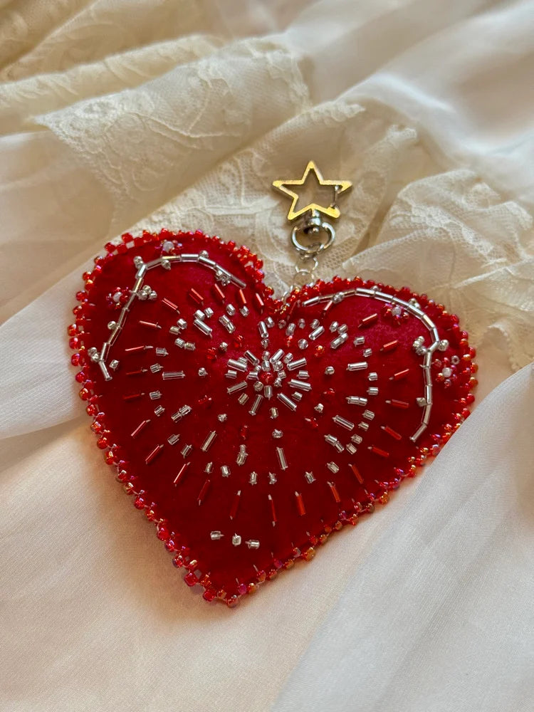 Red heart-shaped embroidered item with a gold star charm on a beige fabric background