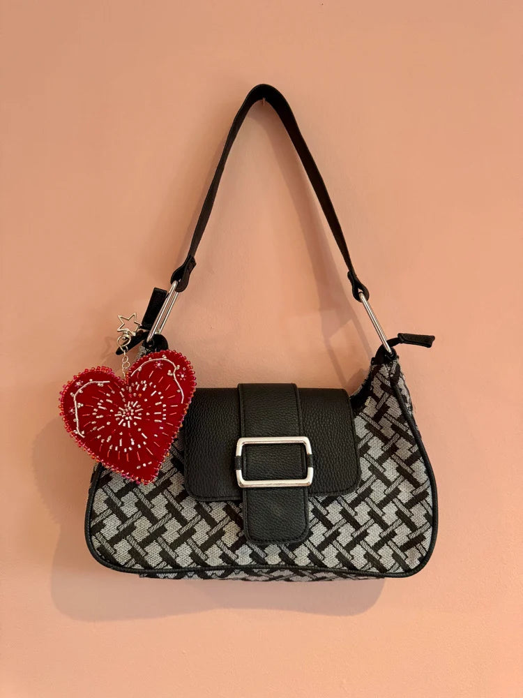 Black and white patterned handbag with a red heart-shaped keychain on a peach background
