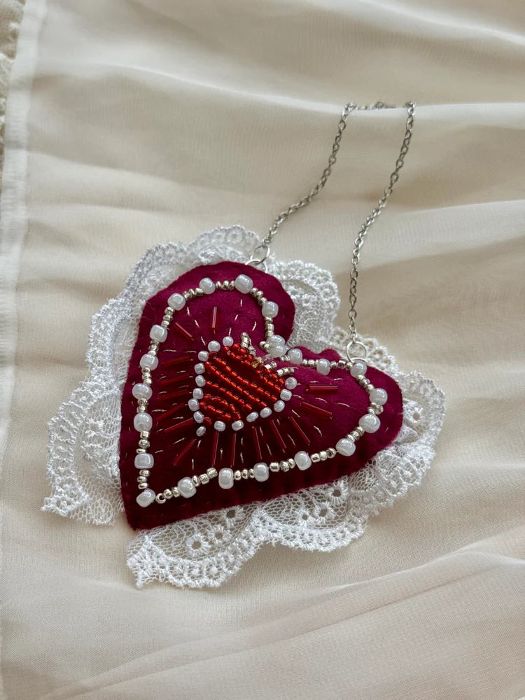 Heart-shaped embroidered pendant with lace details on a beige fabric background