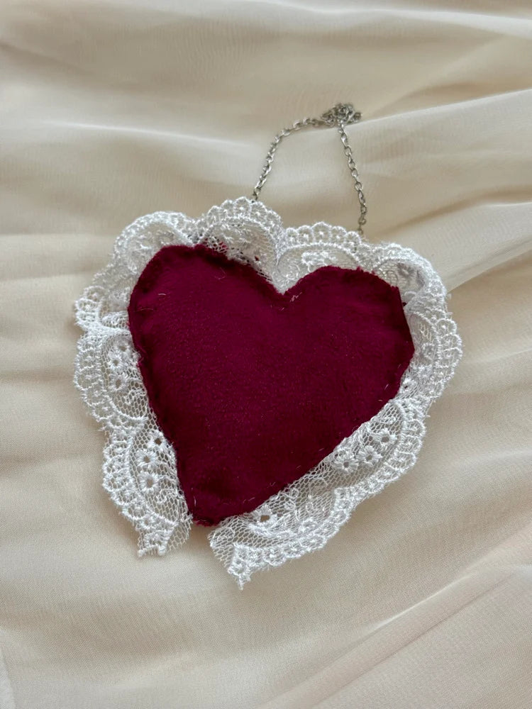 Heart-shaped fabric pendant with lace border on a beige fabric background
