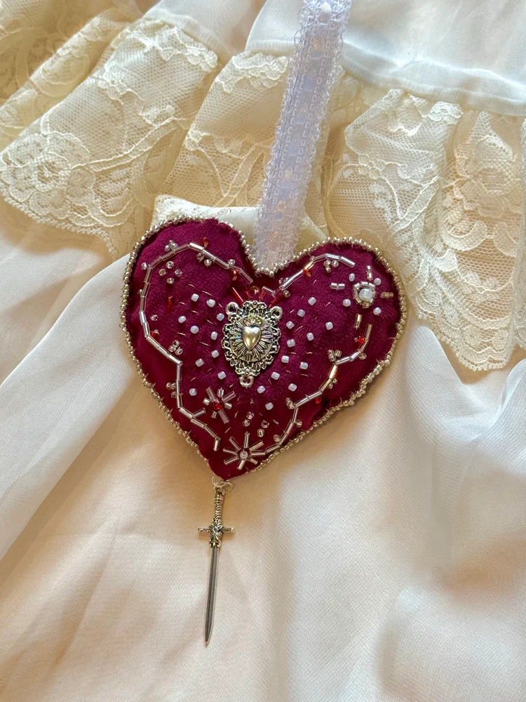 Heart-shaped ornament with scared heart design with a sword on a lace background