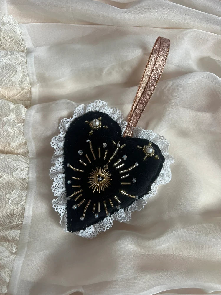 Black heart-shaped decorative item with gold embroidery on a beige fabric background