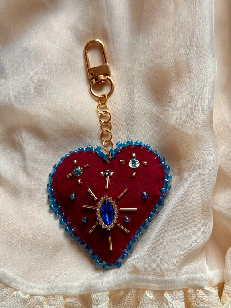 Heart-shaped keychain with blue beads and a gold clasp on a beige fabric background