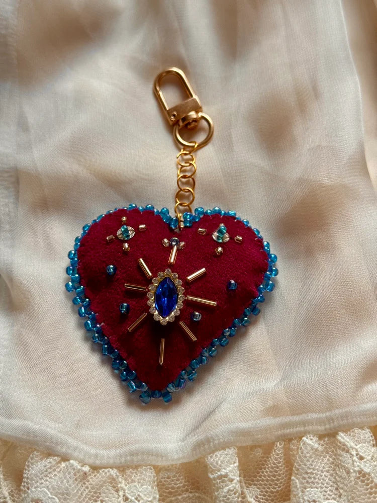 Heart-shaped keychain with red fabric and blue beads on a beige fabric background