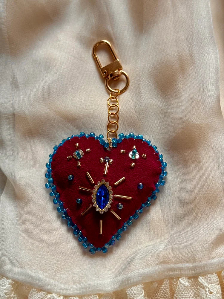 Heart-shaped keychain with red fabric and blue beads on a beige fabric background