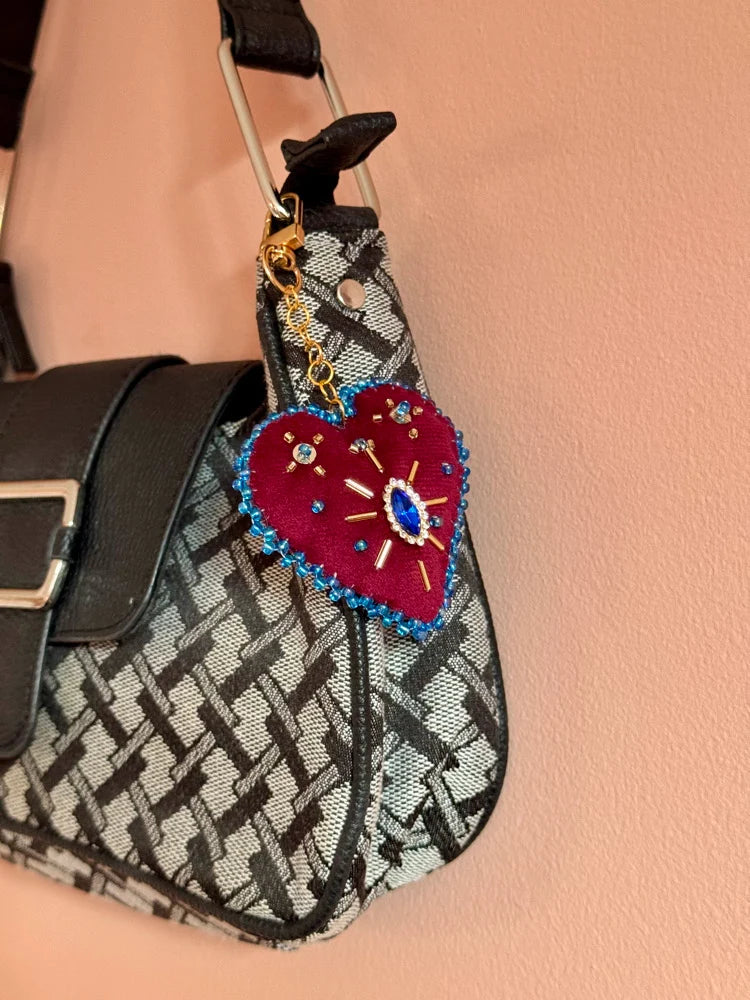 Heart-shaped keychain with colorful details attached to a patterned handbag.