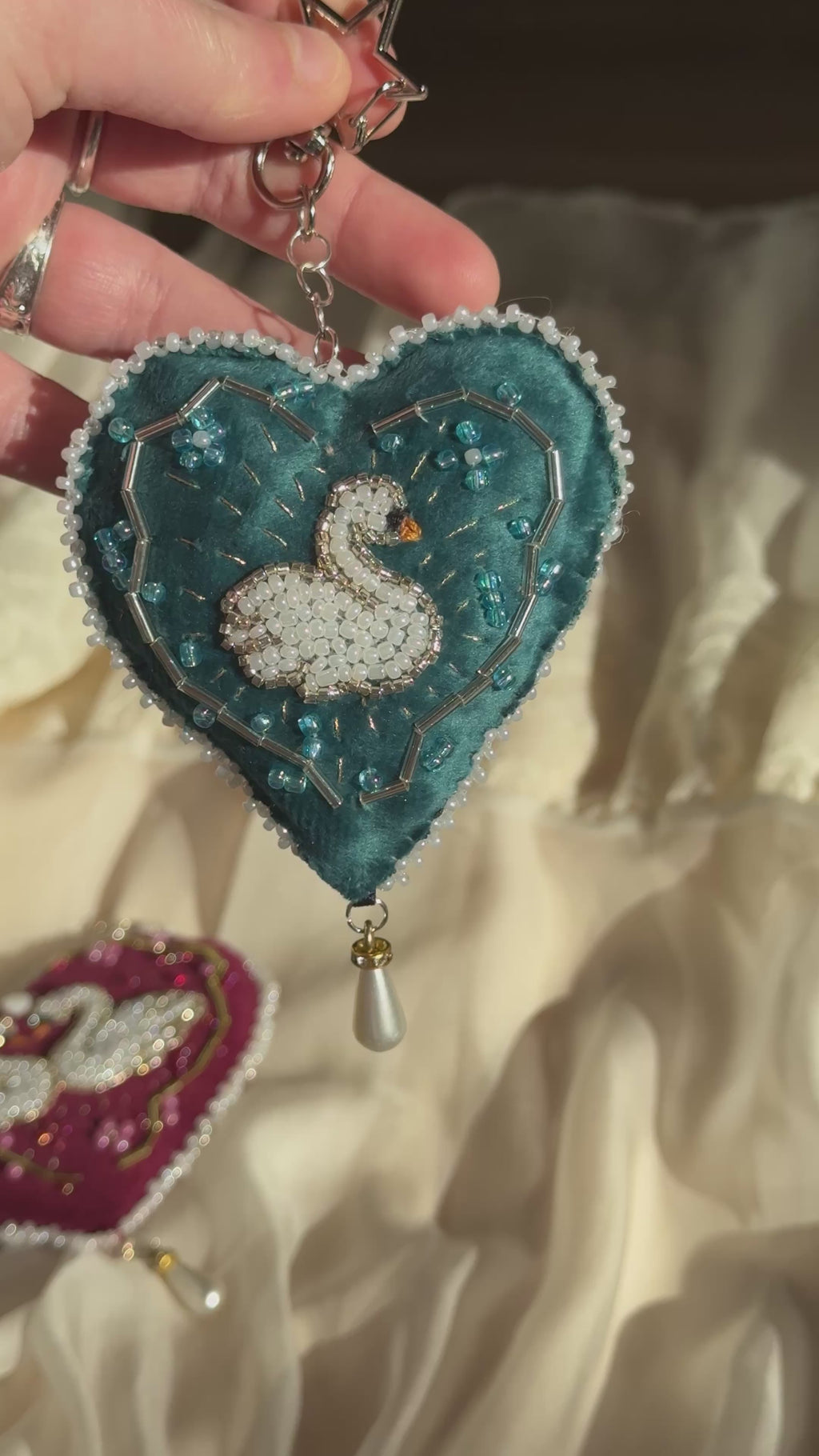 Blue heart shaped velvet bag charm with swan embroidery with beads catching the sunlight.