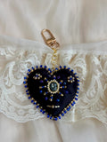 Heart-shaped keychain with blue beads and a gold clasp on a lace background