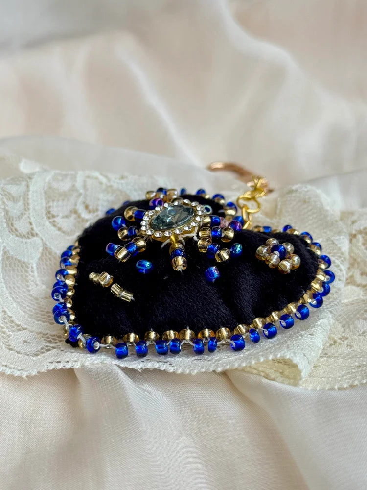 Heart-shaped jewelry chain with blue and gold beads on a lace fabric background