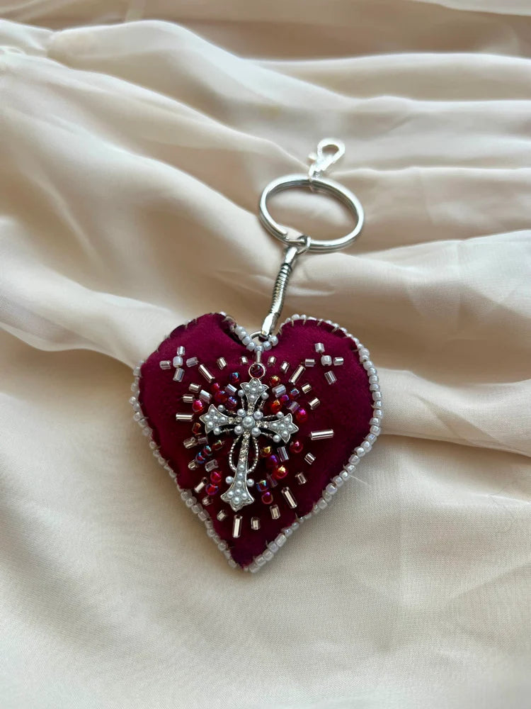 Heart-shaped keychain with bead embellishments on a beige fabric background