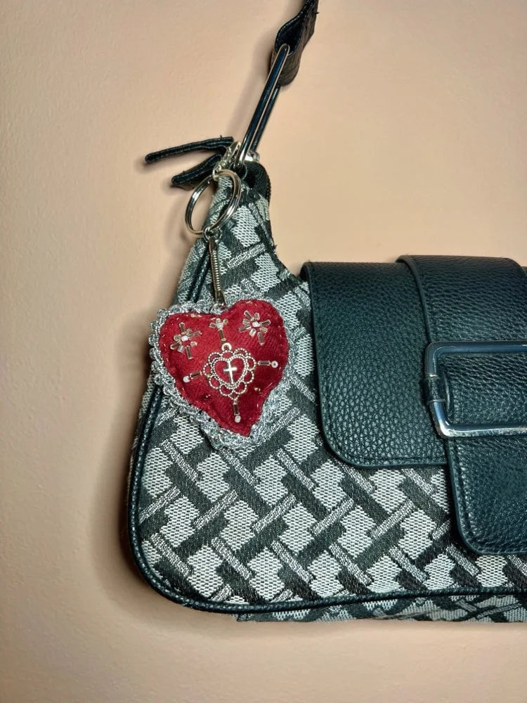 Grey patterned handbag with a red sacred heart design keychain on a beige background