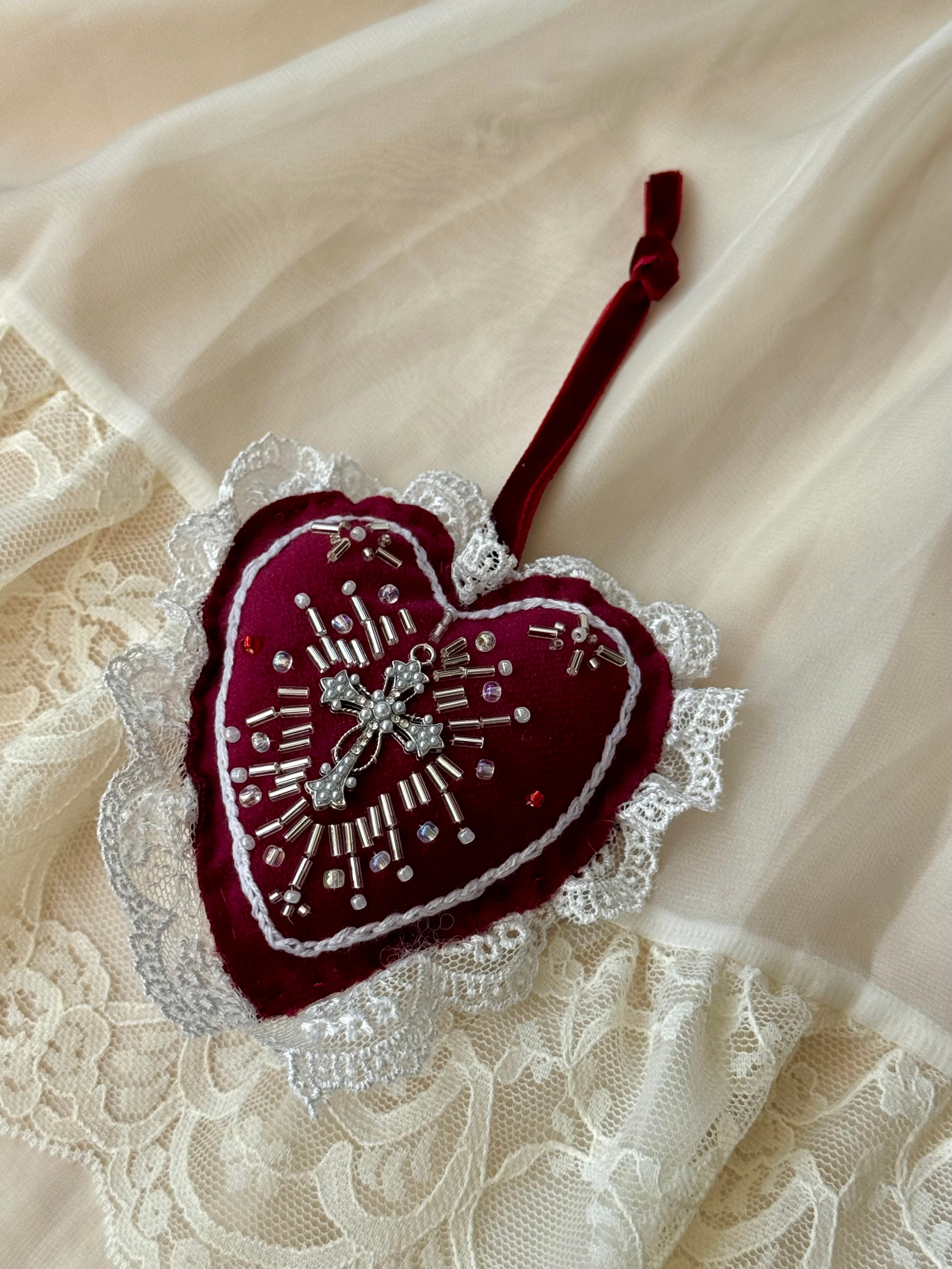 Heart-shaped embroidered decoration with pearls and centre cross on a lace fabric background