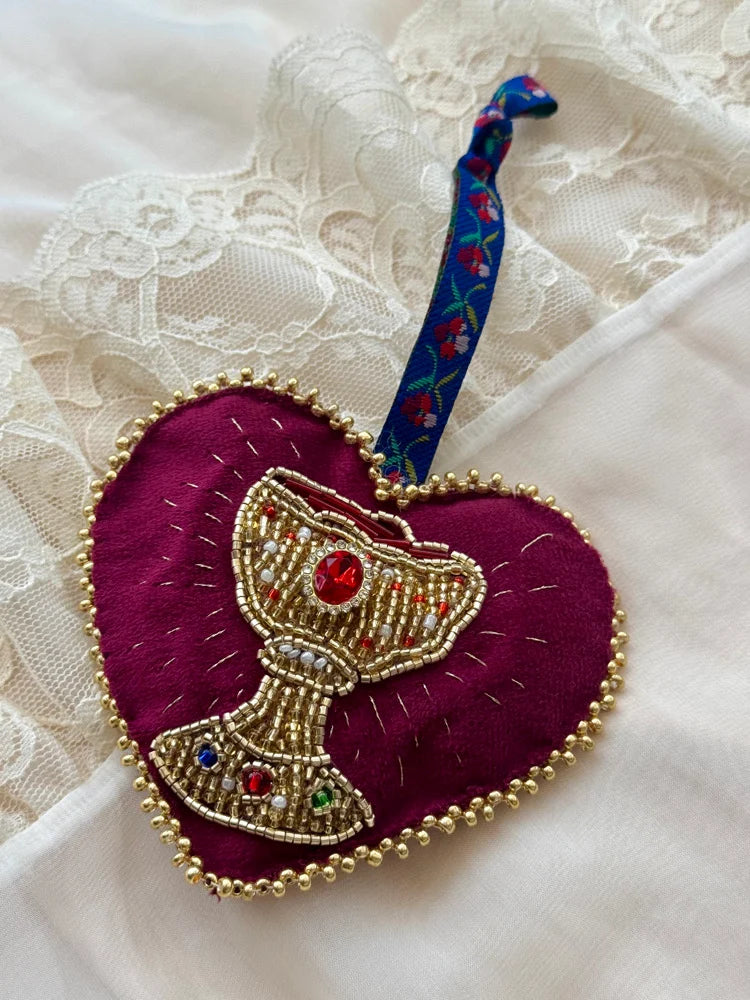 Decorative heart-shaped ornament with a beaded chalice design with floral tie on a lace background