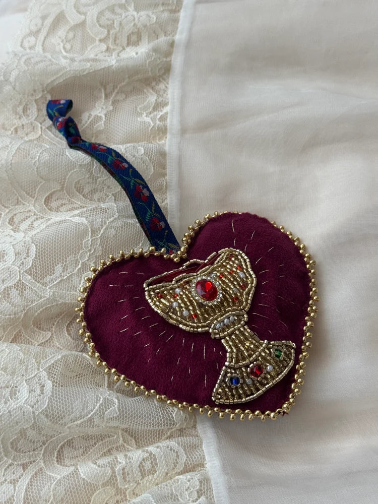 Decorative heart-shaped ornament with a beaded chalice design with floral tie on a lace background