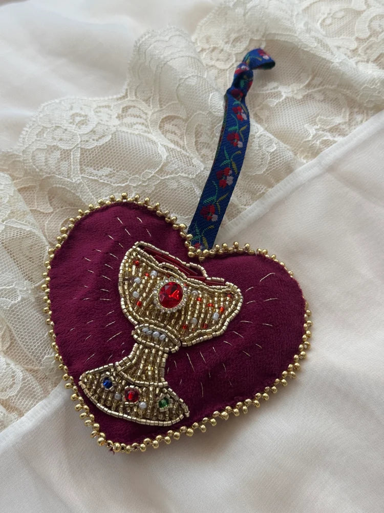 Decorative heart-shaped ornament with a beaded chalice design with floral tie on a lace background