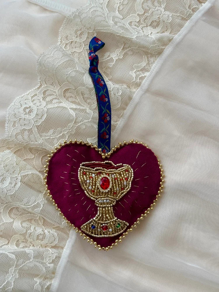 Decorative heart-shaped ornament with a beaded chalice design with floral tie on a lace background