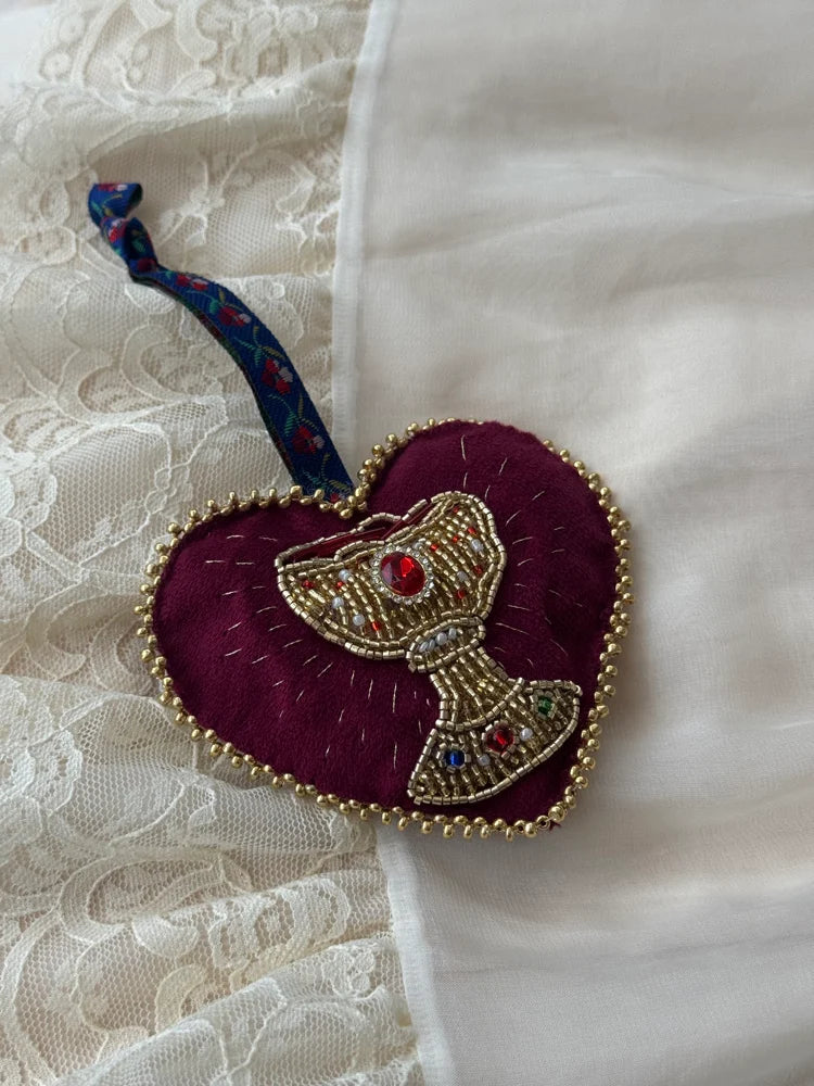 Decorative heart-shaped ornament with a beaded chalice design with floral tie on a lace background