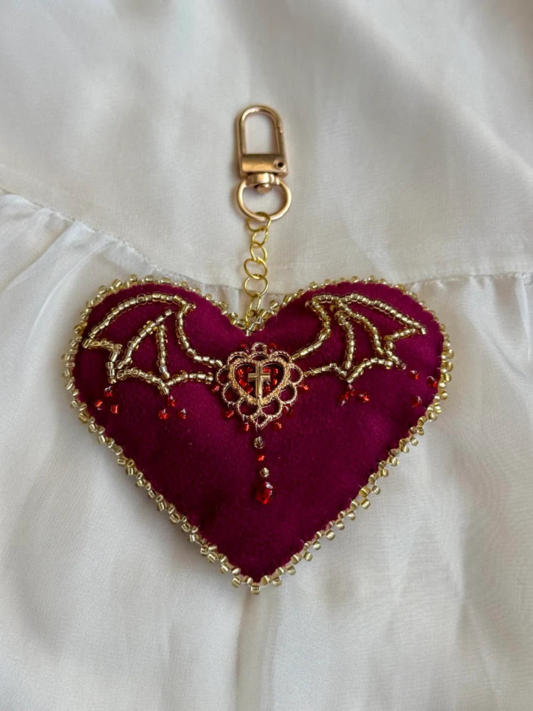 Heart-shaped keychain with gold accents and red stones on a white fabric background