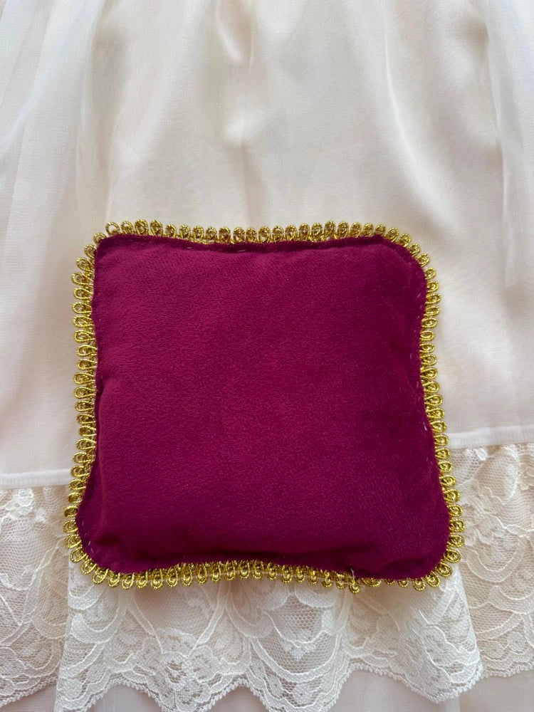 Red velvet cushion with gold trim on a white fabric background
