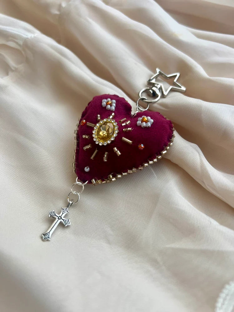 Decorative heart-shaped pendant with star, cross, and intricate design on a soft fabric background