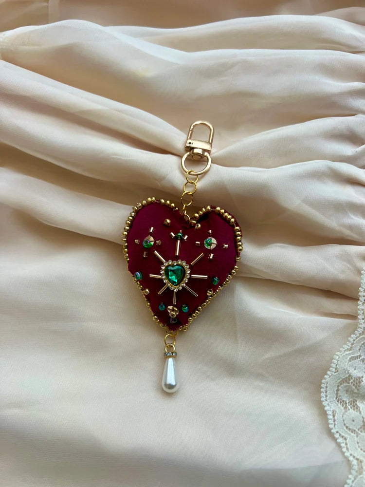Heart-shaped keychain with red background and gold accents on a white fabric background