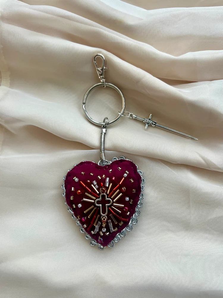 Heart-shaped keychain with decorative elements on a beige fabric background