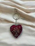 Heart-shaped keychain with decorative elements on a beige fabric background