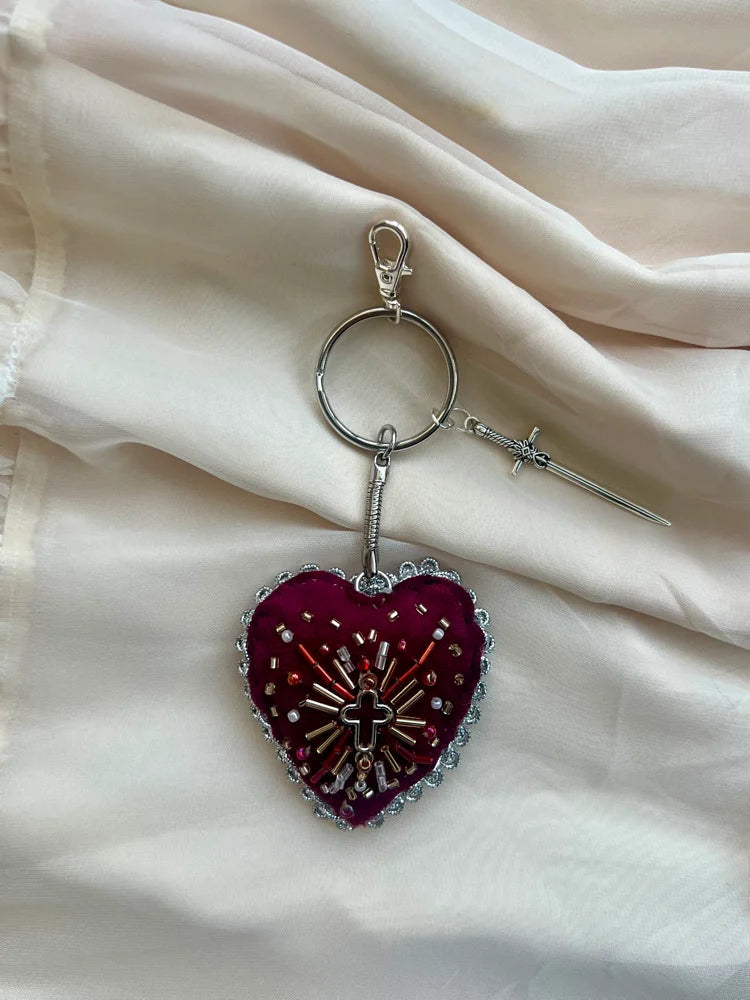 Heart-shaped keychain with a cross design on a light fabric background