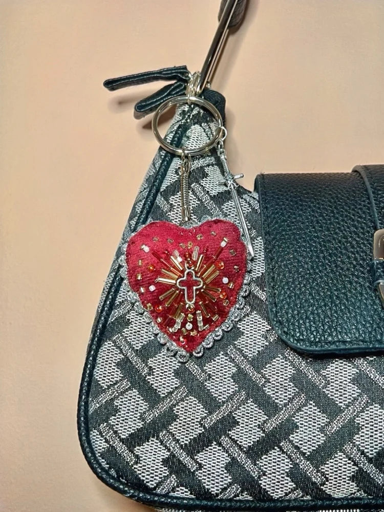 Keychain with sacred heart design and religious cross attached to a checkered bag on a beige background