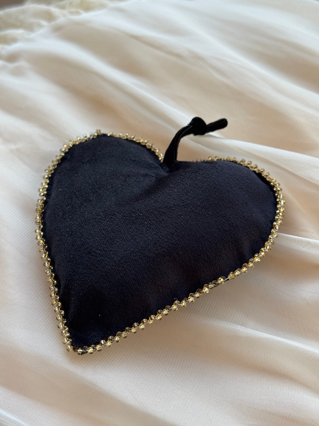 Black heart-shaped ornament with gold beaded edge trim on a white fabric background