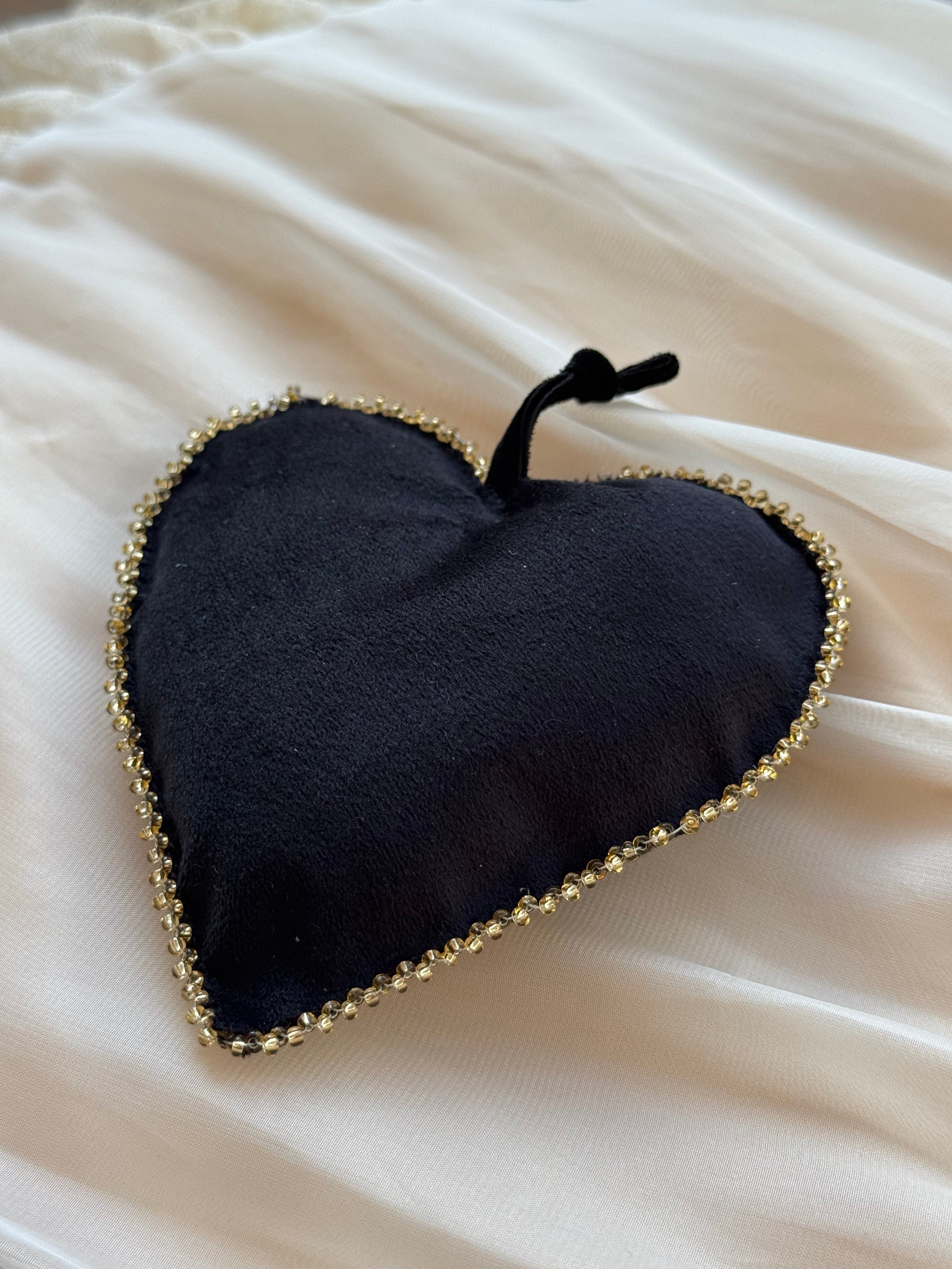 Black heart-shaped ornament with gold beaded edge trim on a white fabric background