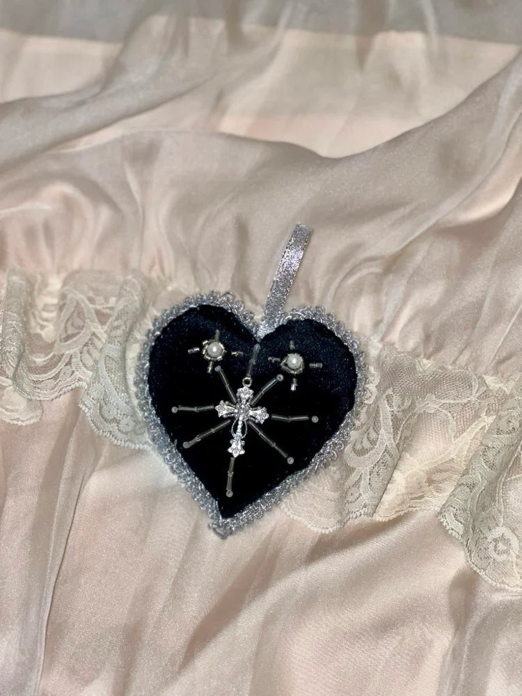 Black velvet heart shaped ornament with silver trim and a cross charm on a satin and lace background