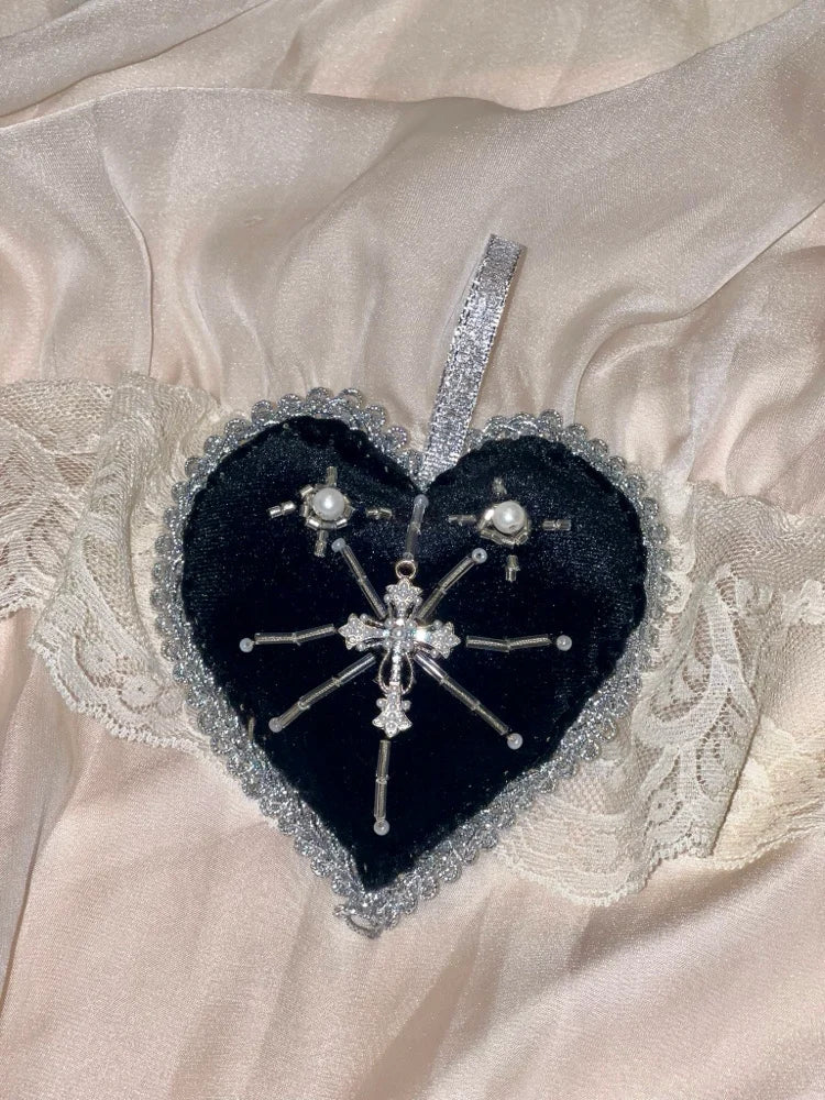 Heart-shaped black pillow with decorative brooches on a textured beige fabric background